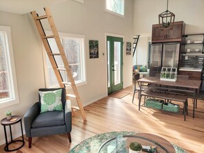 A spacious living room with a wooden ladder, a dining area with a table and benches, and a green door.
