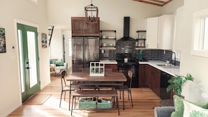 Una cocina moderna con armarios de madera, un refrigerador de acero inoxidable, una estufa negra y una mesa de comedor de madera con sillas.