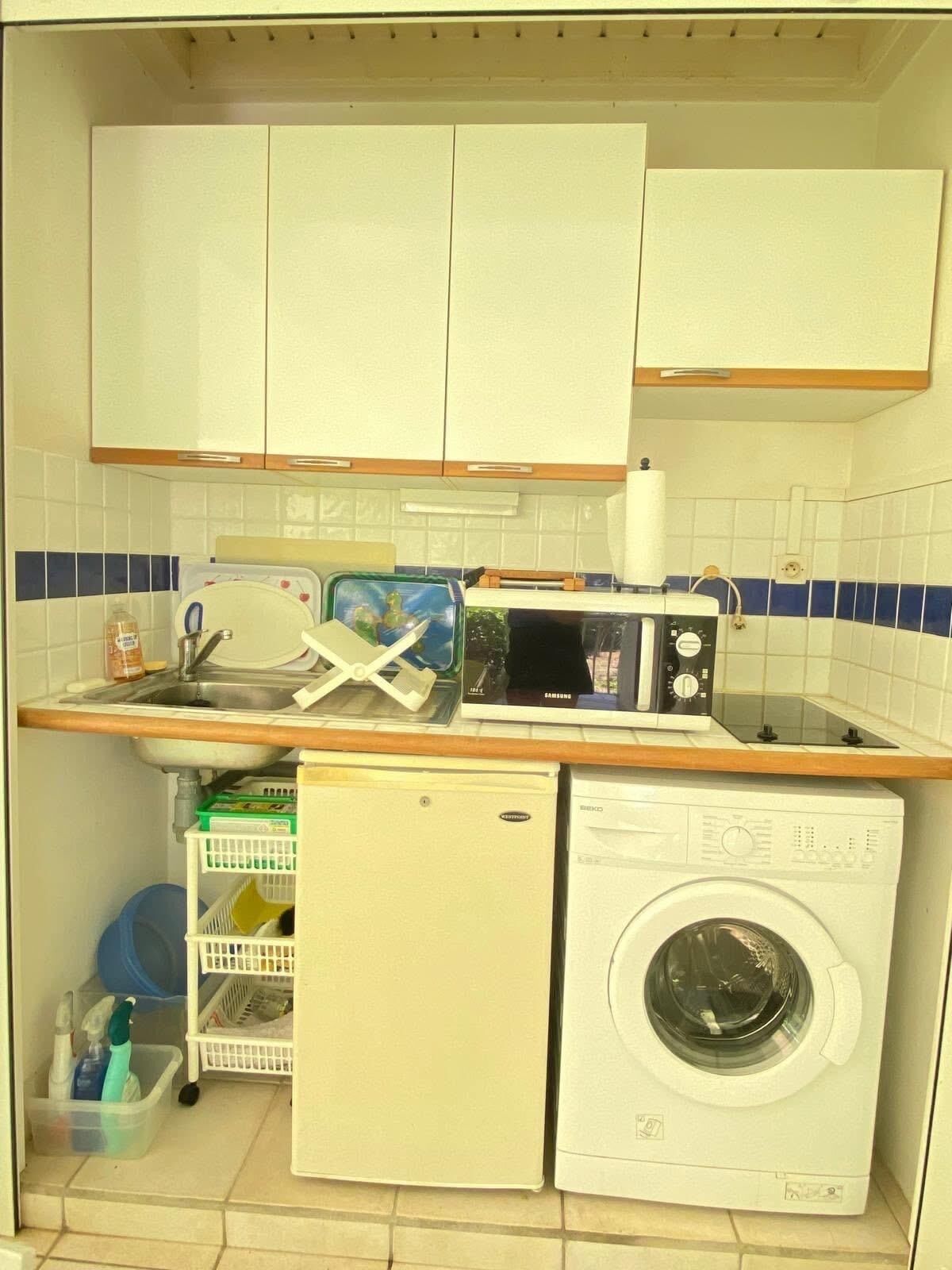 Une cuisine compacte équipée d’un lave-linge, d’un four à micro-ondes et d’un évier.