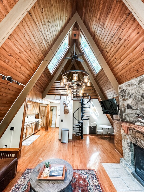 A spacious attic room with wooden walls, a stone fireplace, a dining area, and a kitchen.