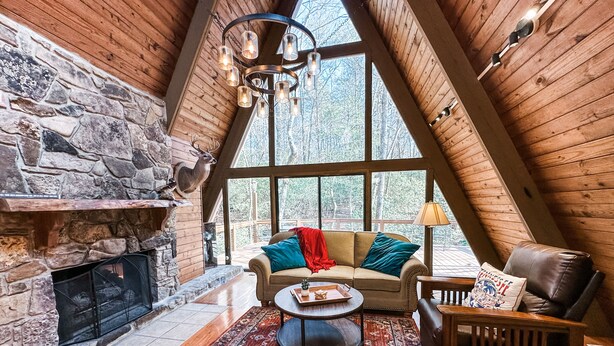 Een gezellig cabin interieur met een stenen openhaard, houten plafond en grote ramen met uitzicht op het bos.