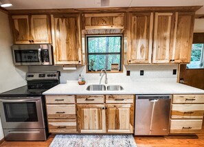 A kitchen with wooden cabinets, stainless steel appliances, and a window with a view of trees.