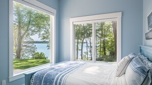 A bedroom with a bed, two windows, and a view of a lake and trees. - Luxurious island home on the water, 30 minute ferry ride from Portland Maine (Portland)