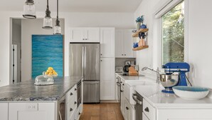 A modern kitchen with white cabinets, a stainless steel refrigerator, a blue mixer, and a large window. - Luxurious island home on the water, 30 minute ferry ride from Portland Maine (Portland)