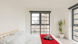 Ett modernt hotellrum med en stor säng, en röd pläd, en krukväxt och utsikt över staden genom ett stort fönster.