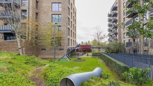 Ett modernt bostadskomplex med en grön innergård, en röd byggnad och en stor, cylindrisk skulptur.