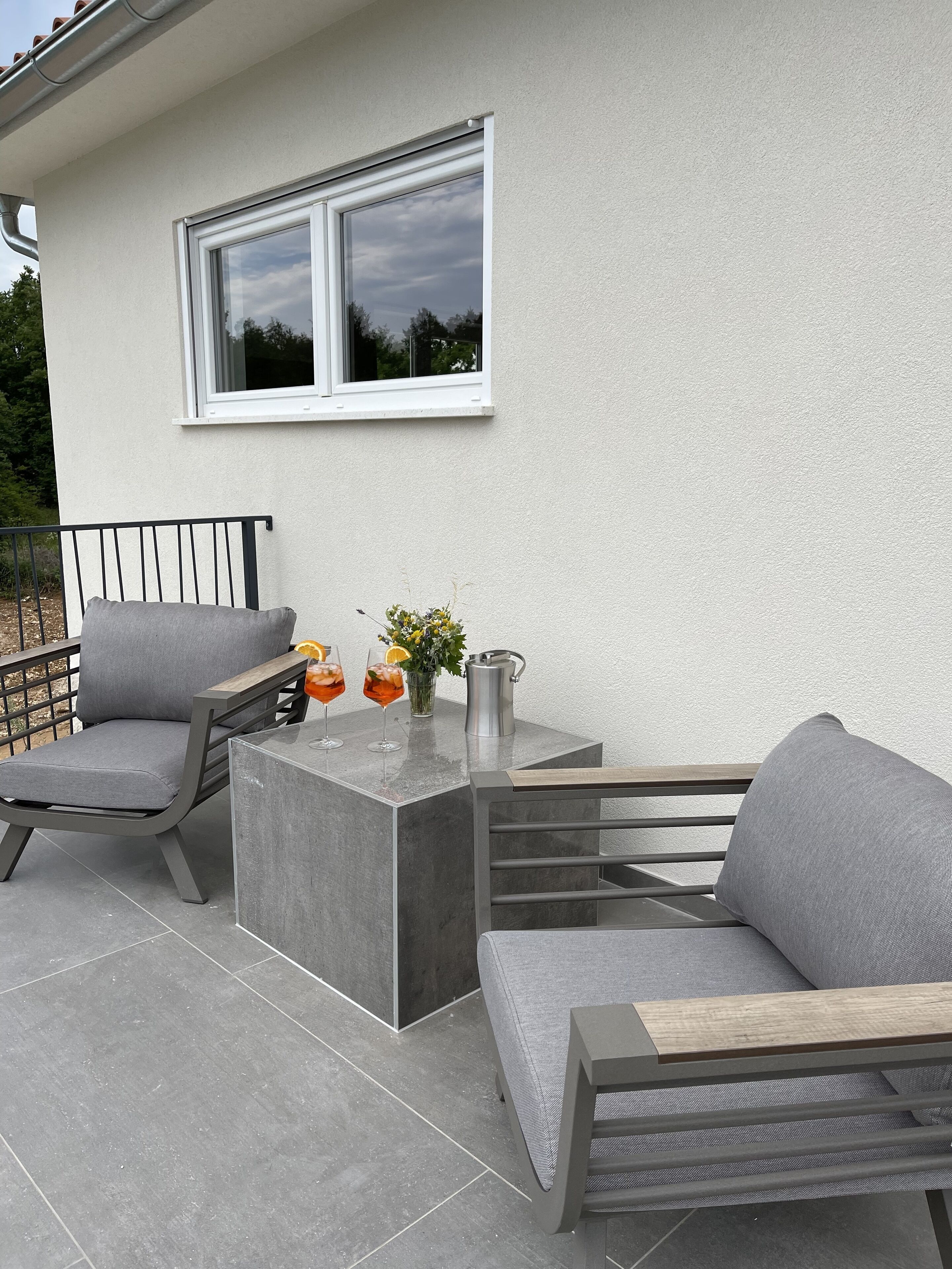 Ett utomhusområde med sittplatser och modern design, med ett bord i betong och två grå soffor med detaljer i trä.