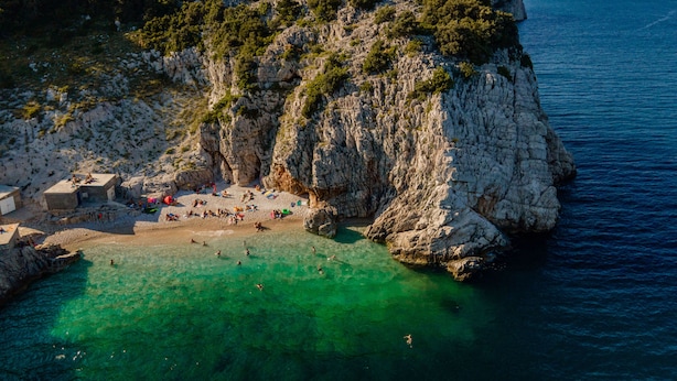 A coastal area with rocky cliffs, clear turquoise water, and a sandy beach.
