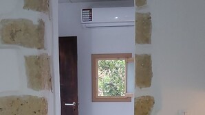 Una stanza con pareti in mattoni a vista, una porta in legno, una piccola finestra che si affaccia sul verde e un soffitto bianco.