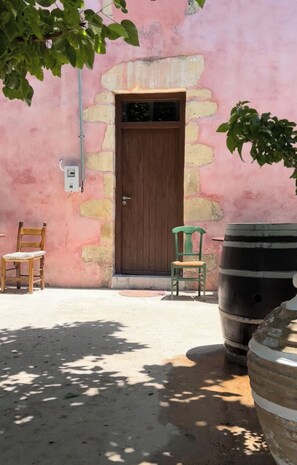 A pink building with a wooden door, two chairs, and a large barrel.