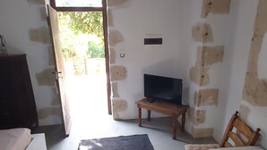 Una stanza con parete in pietra, un tavolo di legno, una televisione su un mobile e una porta che dà sull'esterno.