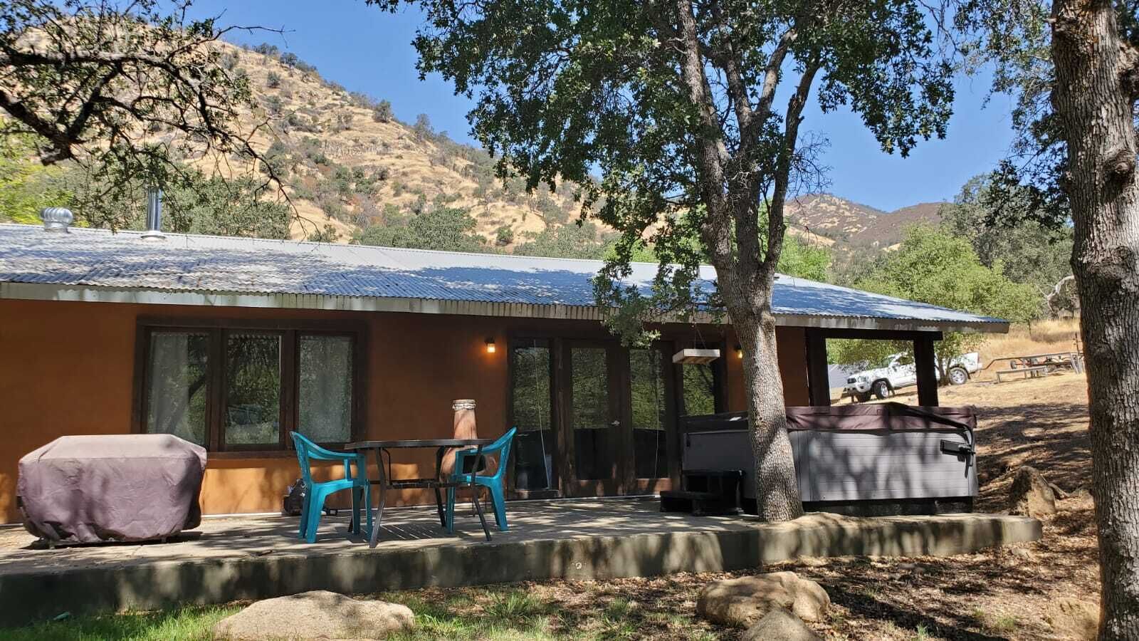 A rustic cabin with a covered patio, outdoor seating, and a vehicle parked nearby.