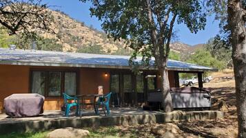 A rustic cabin with a covered patio, outdoor seating, and a vehicle parked nearby.