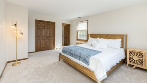 A bedroom with a wooden bed, a nightstand, a floor lamp, and a door. - Cozy 5-bedroom with lake views and spacious deck (Westmont)