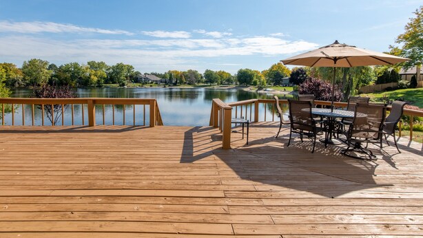 A wooden deck with a table and chairs, overlooking a calm lake with trees in the background. - Cozy 5-bedroom with lake views and spacious deck (Westmont)
