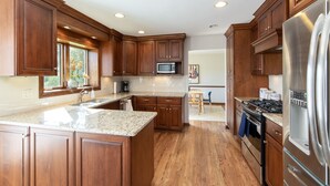 A kitchen with wooden cabinets, granite countertops, a stainless steel refrigerator, and a built-in microwave. - Cozy 5-bedroom with lake views and spacious deck (Westmont)