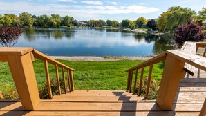 A wooden deck leading to a lake with a grassy area and trees in the background. - Cozy 5-bedroom with lake views and spacious deck (Westmont)