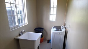 A small, clean bathroom with a white sink, a washing machine, and a window. - Loodik Vacation Home Brompton Manor  (Speculation)