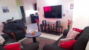 A living room with two black sofas, a small round table, a flat-screen TV, and a kitchen area in the background. - Loodik Vacation Home Brompton Manor  (Speculation)
