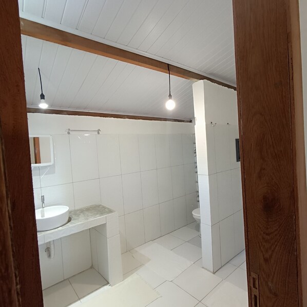 A bathroom with white tiles, a sink, a toilet, and two pendant lights.