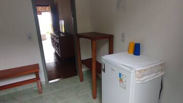 A compact room with a refrigerator, a wooden bench, a small table, and a door leading to another room.