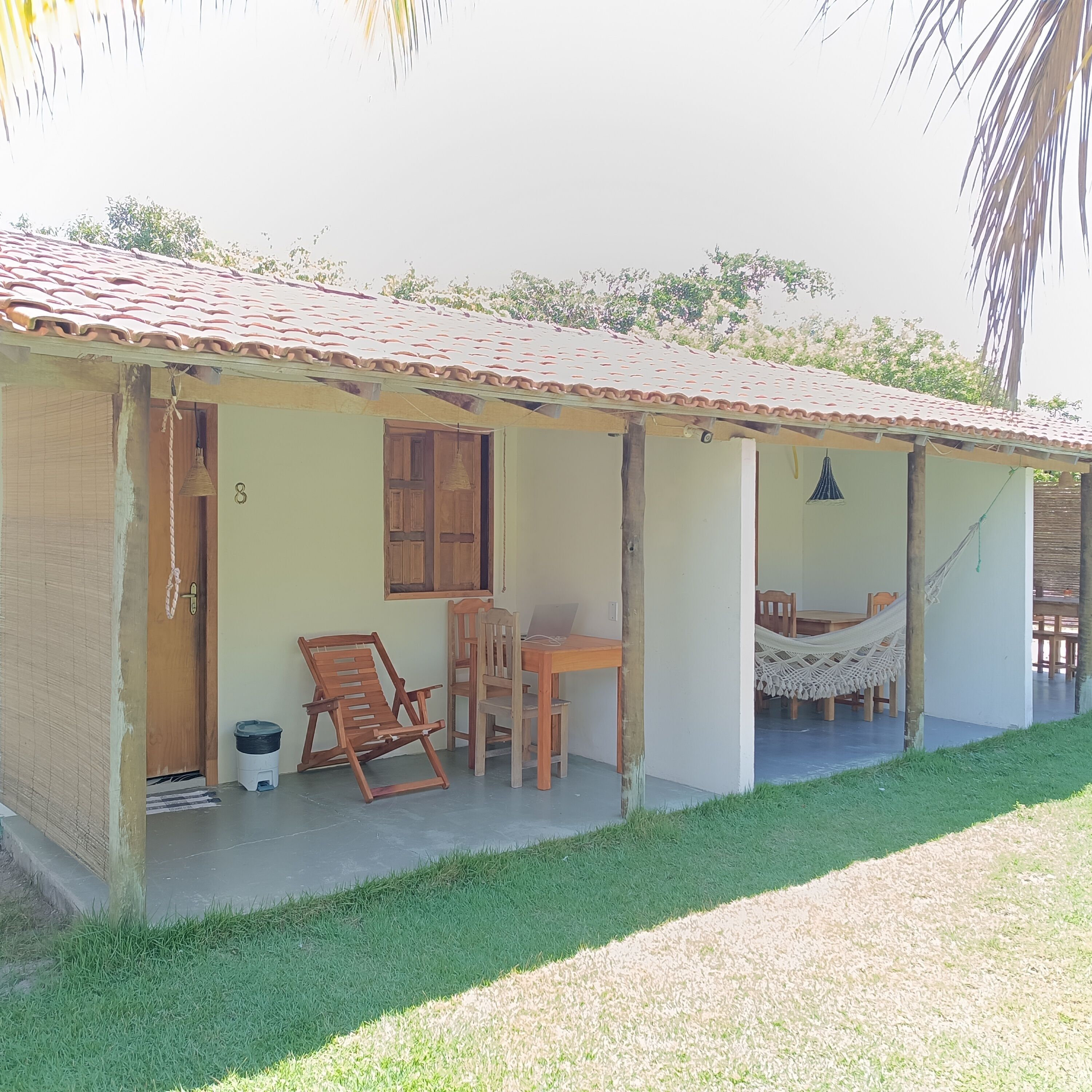 Una casa de un piso con techo de tejas, un porche con mobiliario de madera y una hamaca.