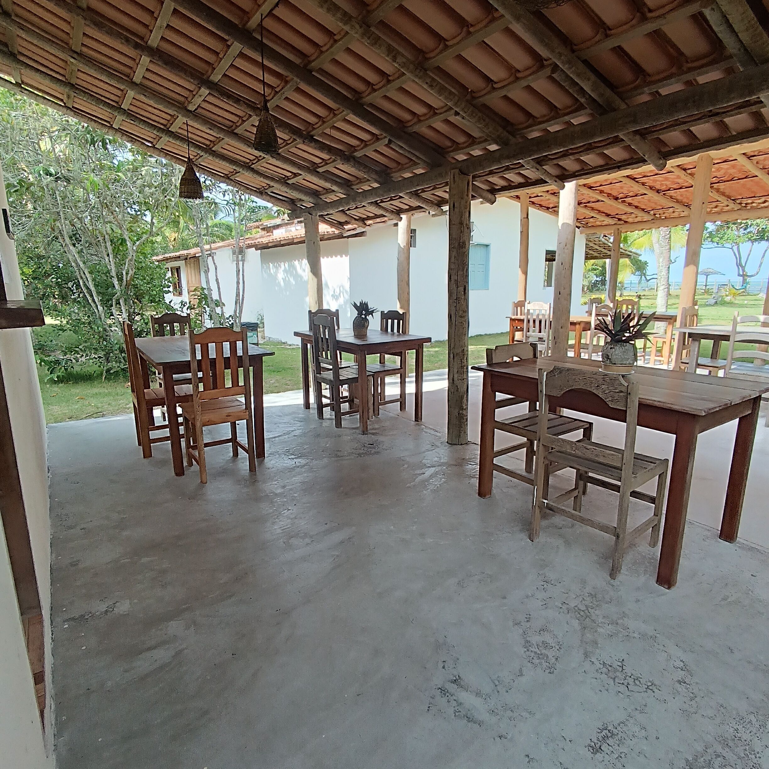 An outdoor covered patio with wooden furniture and a concrete floor.