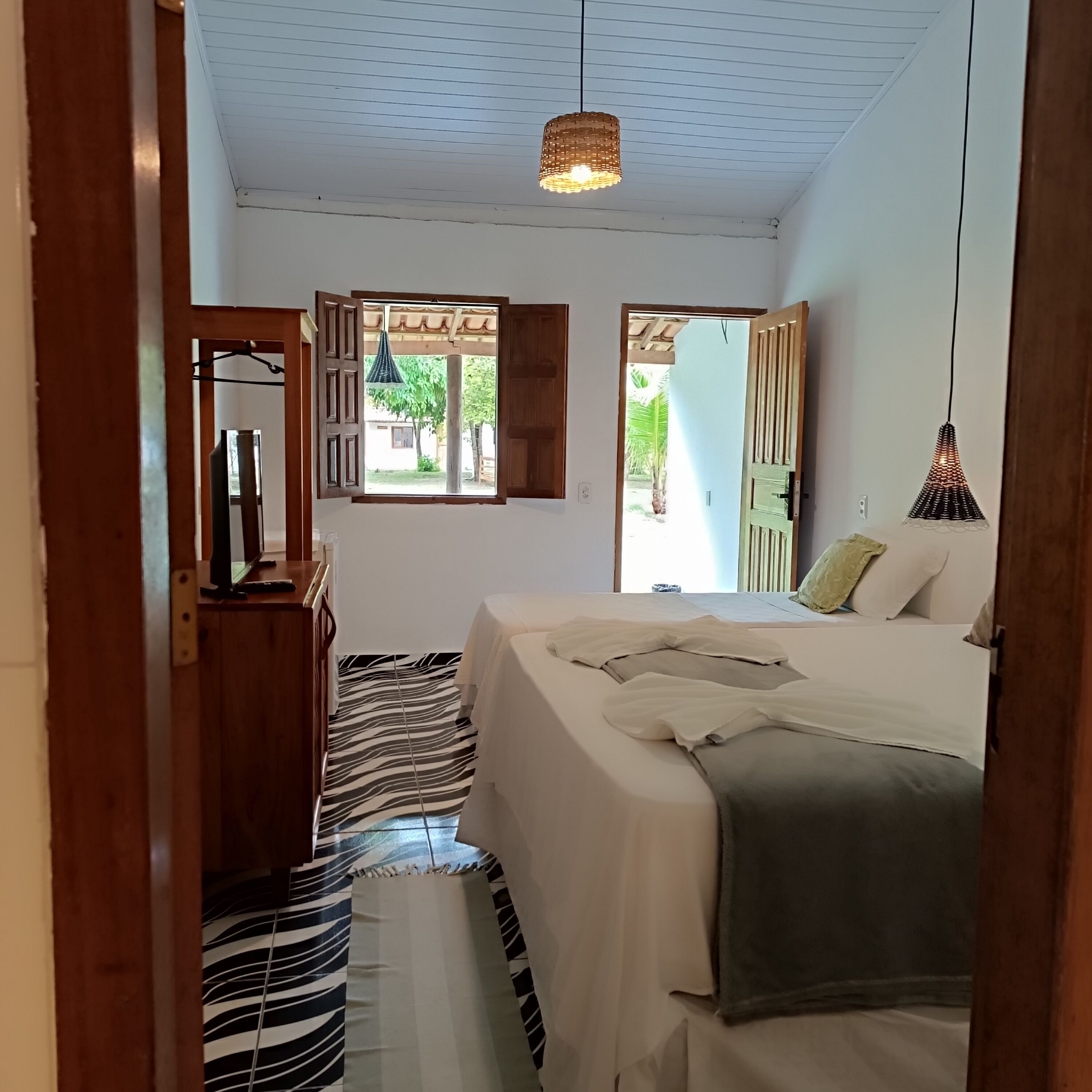 A bedroom with a bed, a window, a hanging light fixture, and a patterned rug.