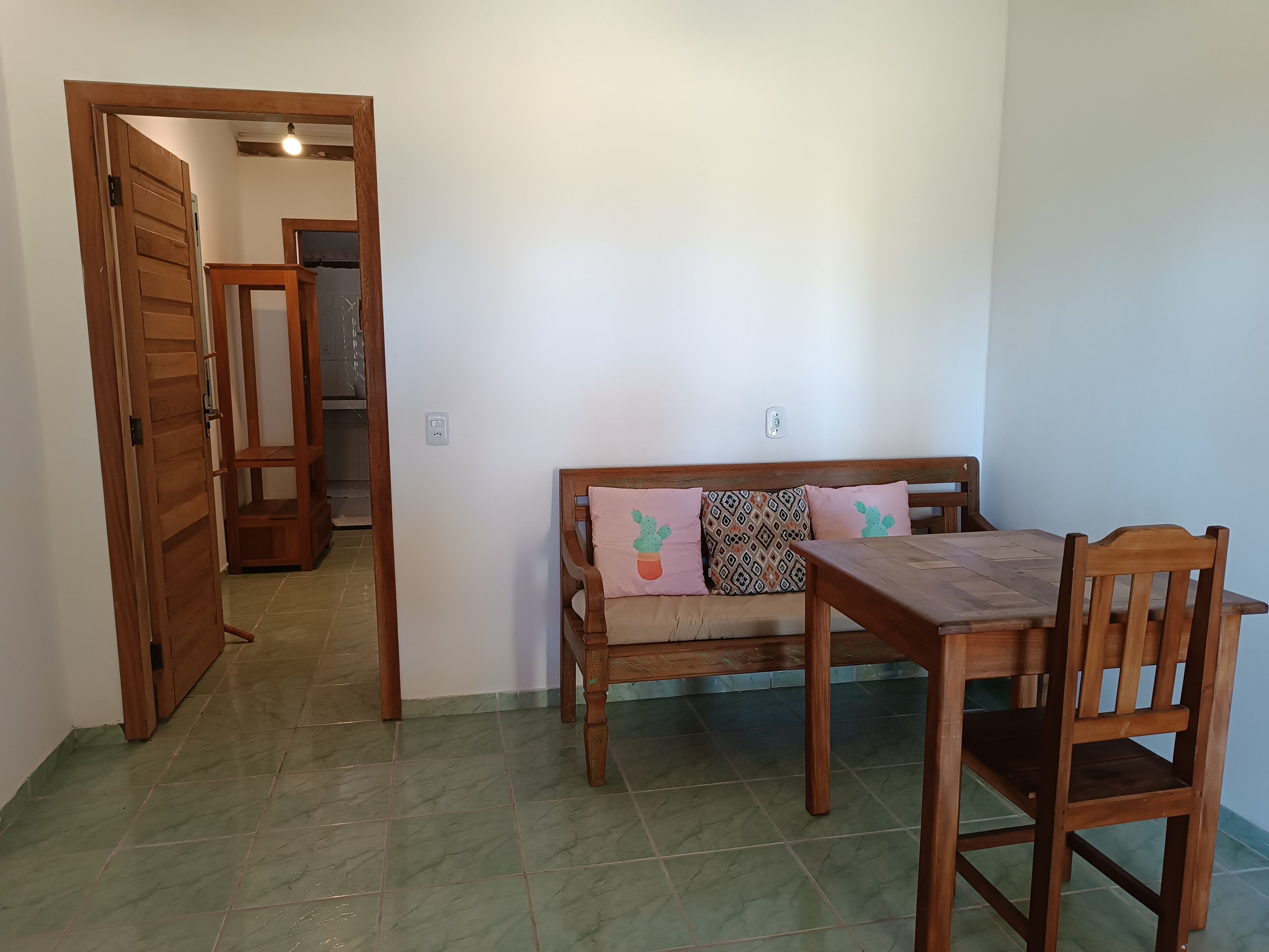 A dining area with a wooden table and bench, a wooden door leading to another room, and a tiled floor.