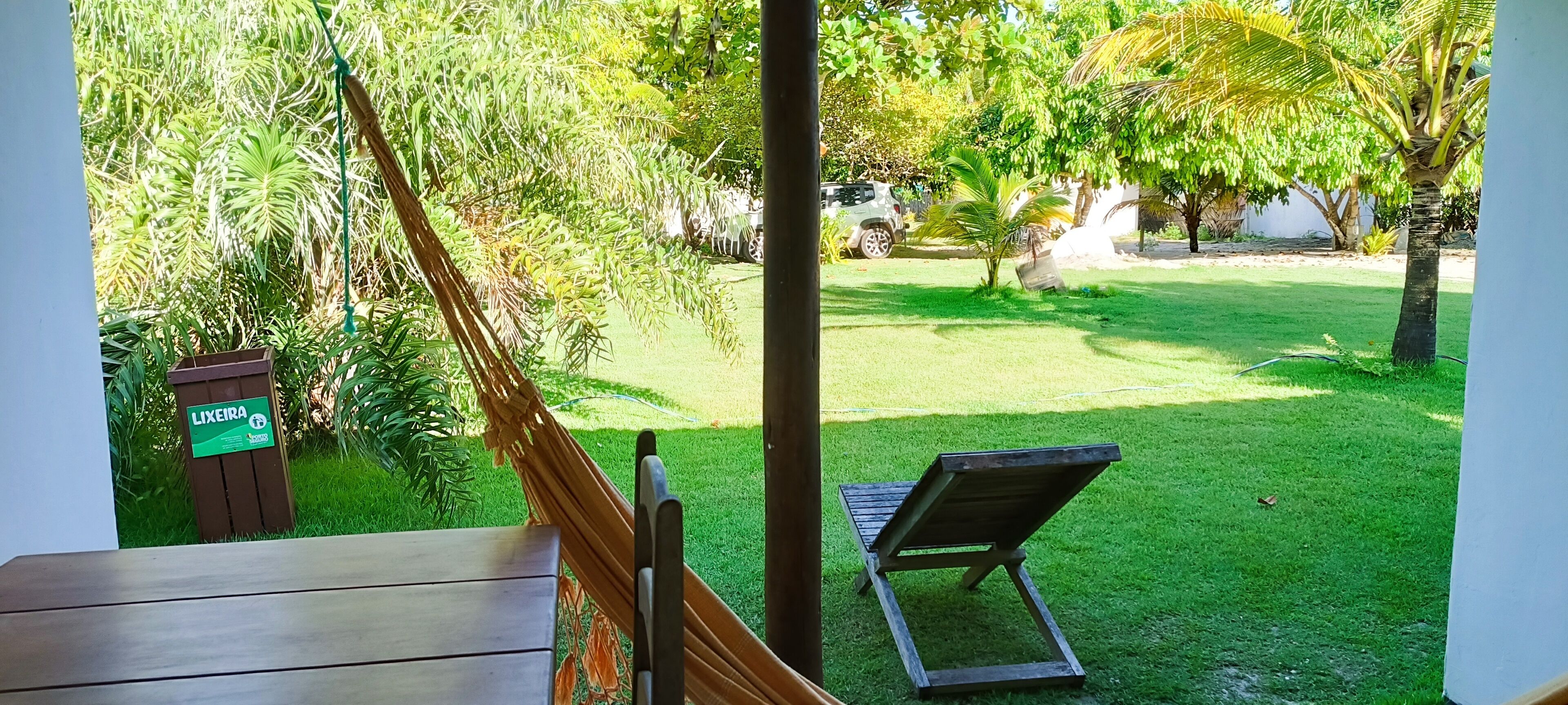A view from a balcony overlooking a well-maintained lawn with a wooden bench and a sign labeled "LIXEIRA."