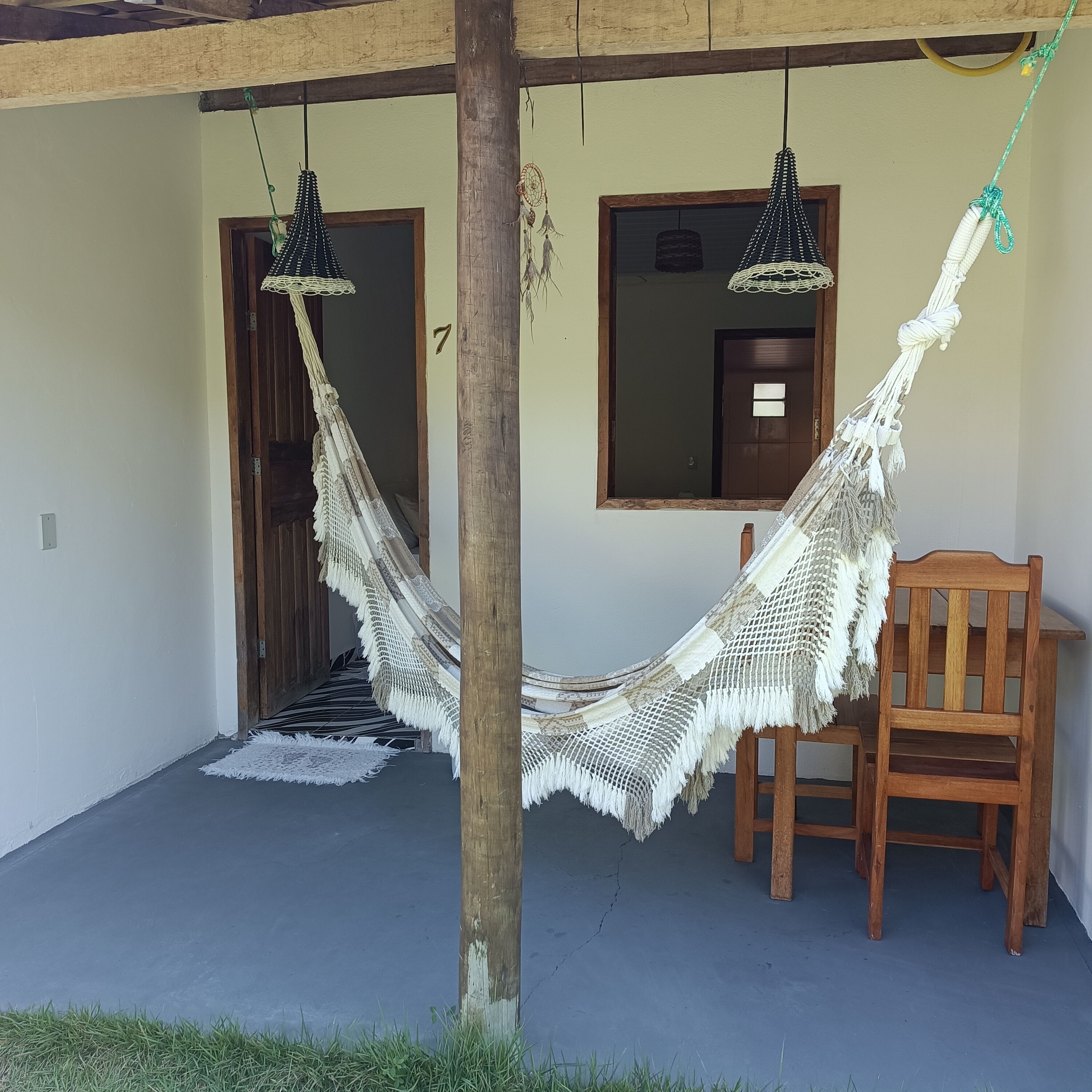 Una silla hamaca colgada de una viga de madera, una silla de madera y una puerta con ventanal.