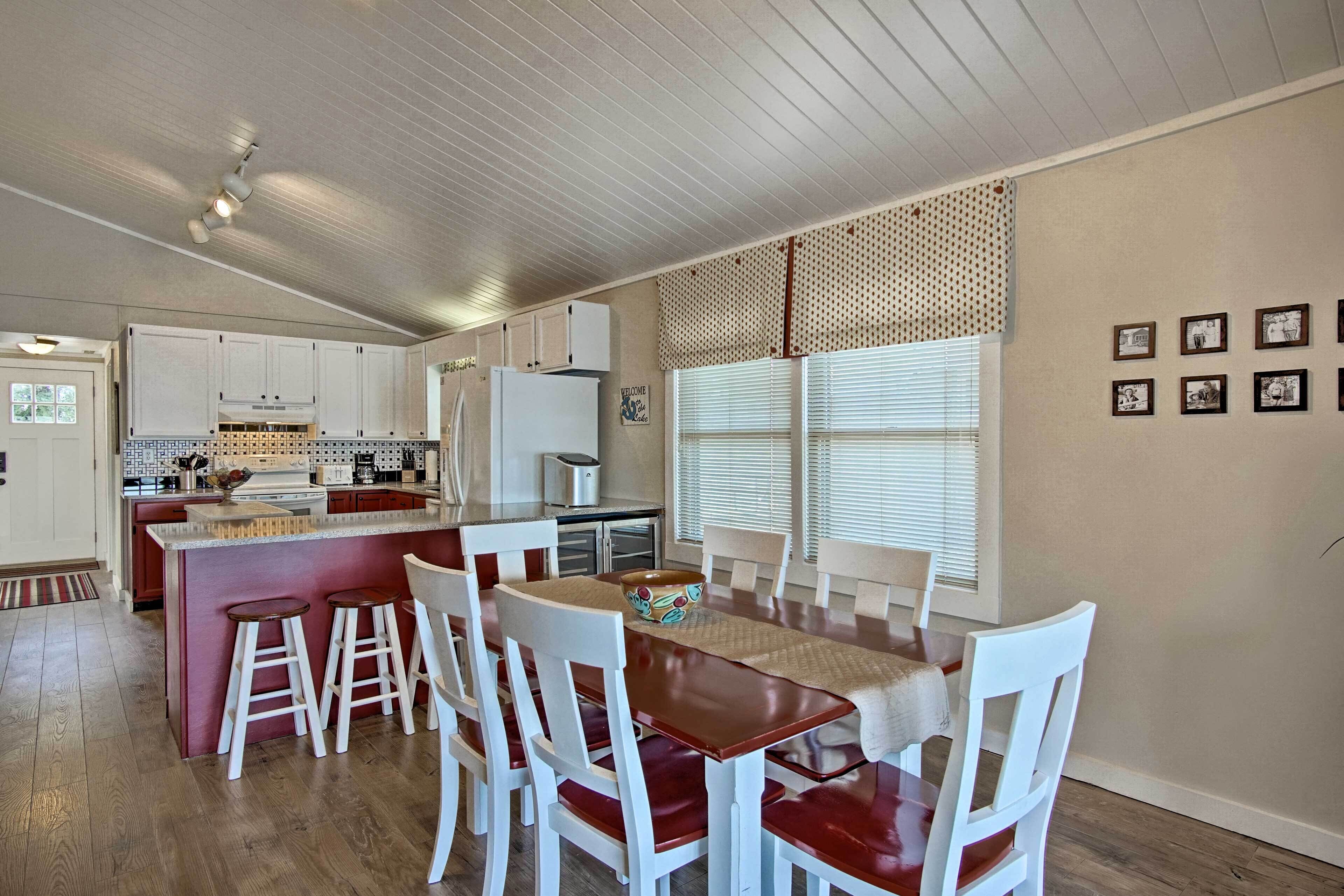 Una cocina con armarios blancos, una isla central con taburetes y una mesa de comedor con sillas.