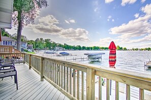 A wooden deck with chairs and a red umbrella, overlooking a calm body of water with boats and a dock. - Cheerful lakefront cottage with kayaks and fire pit (Fremont)