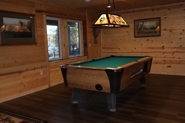 Una mesa de billar en una habitación con paredes de madera y un ventanal.