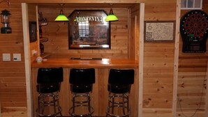 A wooden bar area with three stools, a dartboard, and a framed menu. - Lakefront Cabin on a Private Lake - only a 0.5 mile from the snowmobile trials! (Crandon)