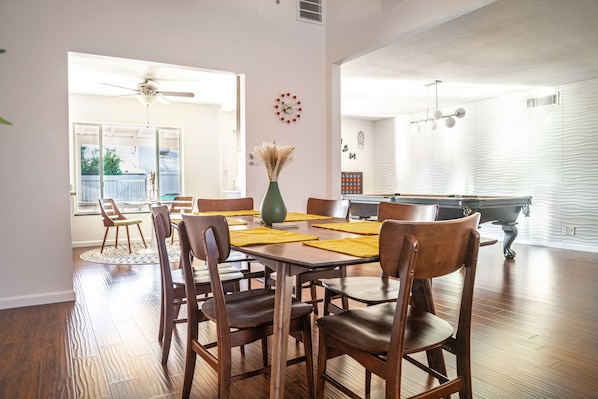 A dining area with a wooden table, chairs, a vase, and a clock on the wall.