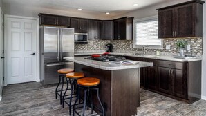 Une cuisine moderne avec des meubles en bois foncé, des appareils électroménagers en acier inoxydable, un îlot central doté de tabourets et un pare-feu en carreaux.