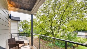 A balcony with wicker furniture, a view of trees, and a fenced area with outdoor equipment. - The Lischey House-East Nashville (Nashville)