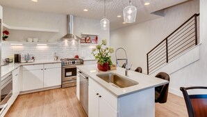 A modern kitchen with white cabinetry, a stainless steel stove, and pendant lighting. - The Lischey House-East Nashville (Nashville)