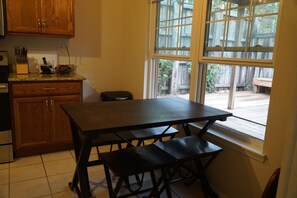 Una cocina con armarios de madera, una encimera con utensilios, una mesa con bancos y una ventana con vistas a una terraza de madera.