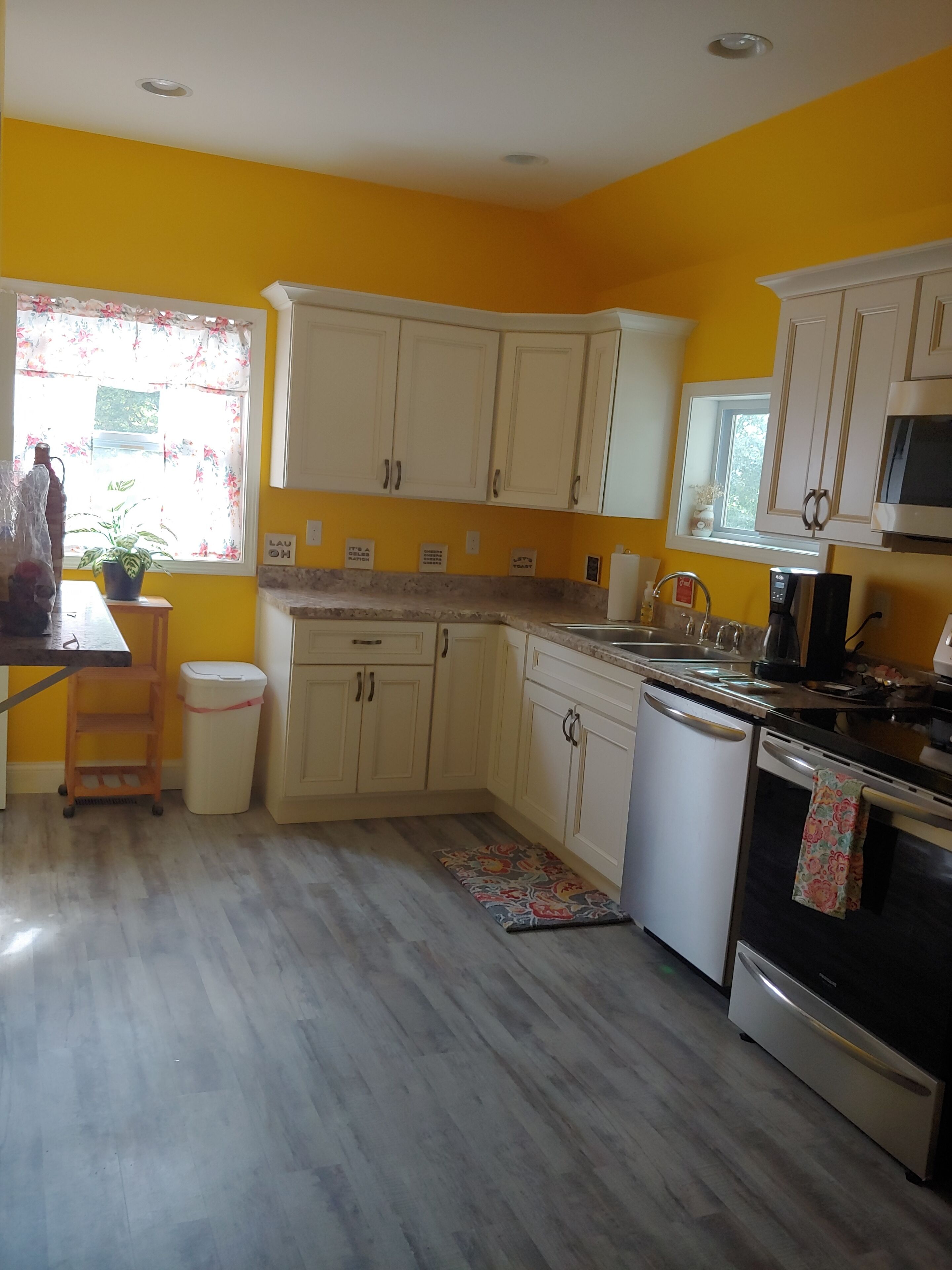 A kitchen with yellow walls, white cabinets, a stainless steel microwave, and a dishwasher.