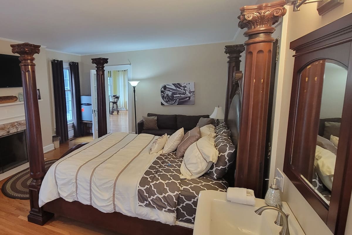 A bedroom with a large bed, a fireplace, a television, and a mirror.