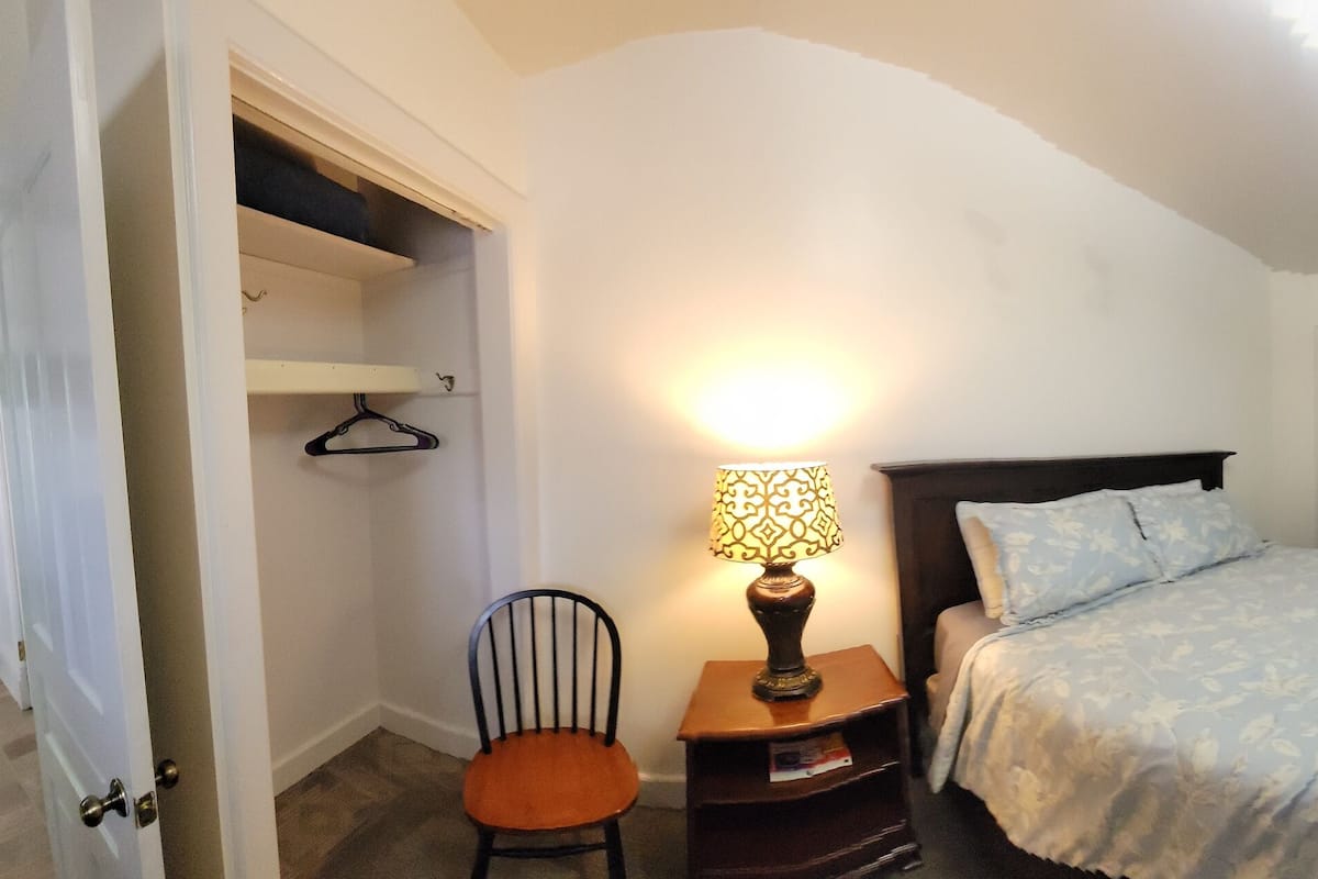 A bedroom with a bed, a chair, a dresser, and a lamp.