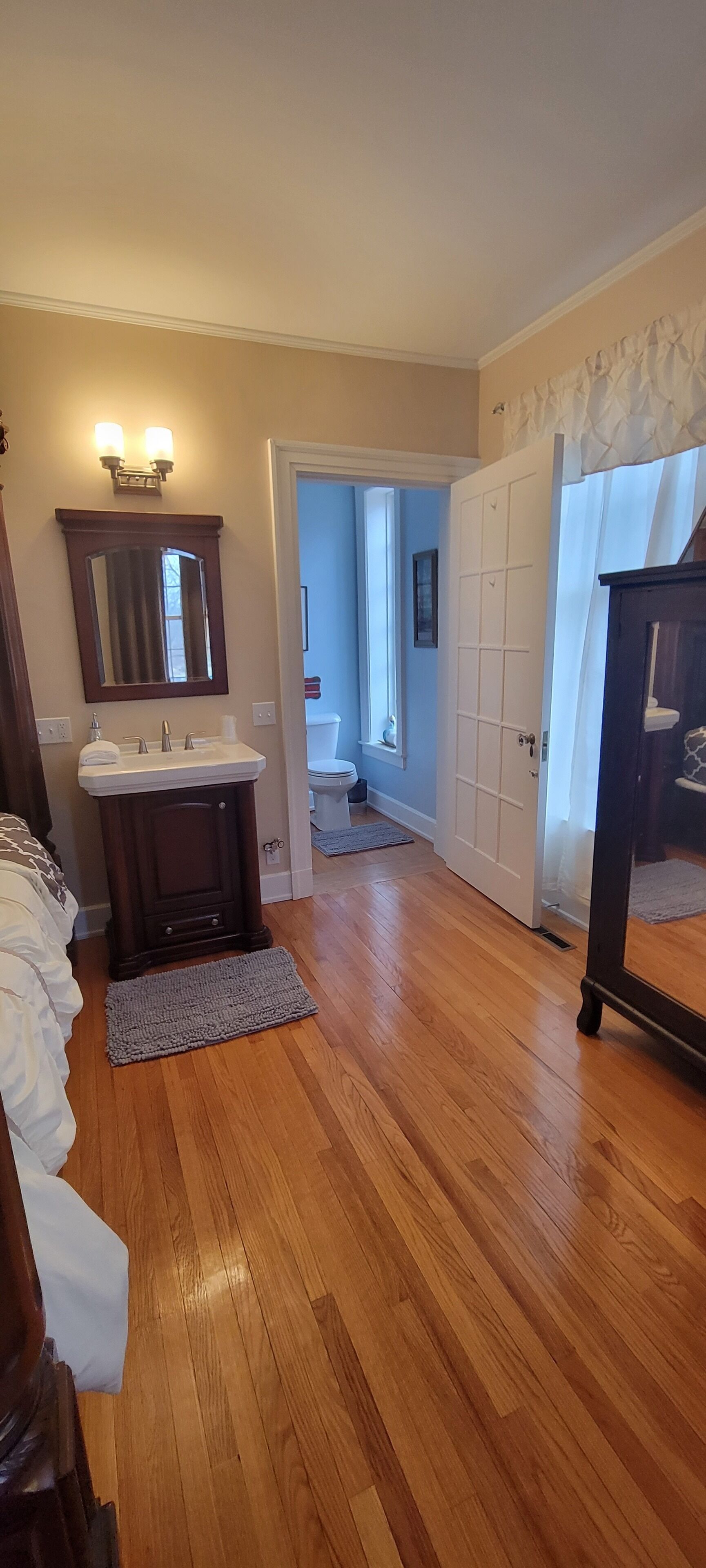 A room with wooden flooring, a white sink, a mirror, and a door leading to another room.