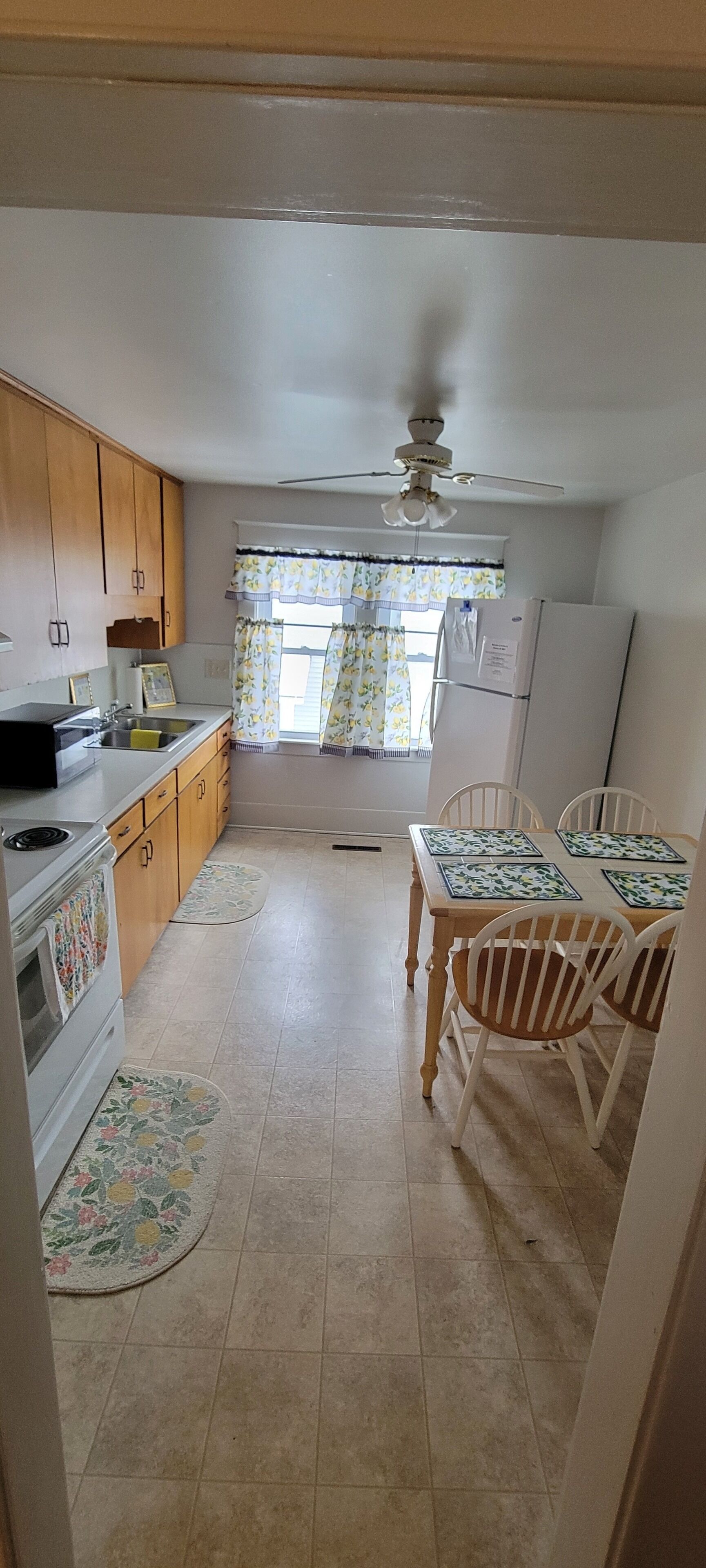 A compact kitchen with wooden cabinets, a refrigerator, a stove, and a dining table with chairs.