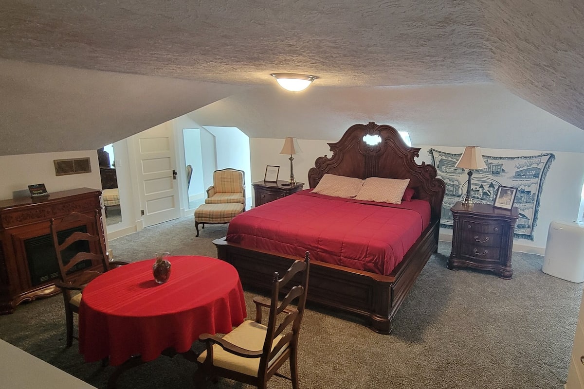 A bedroom with a large bed, a small table, a chair, a dresser, and a nightstand.