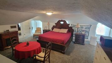 A bedroom with a large bed, a small table, a chair, a dresser, and a nightstand.