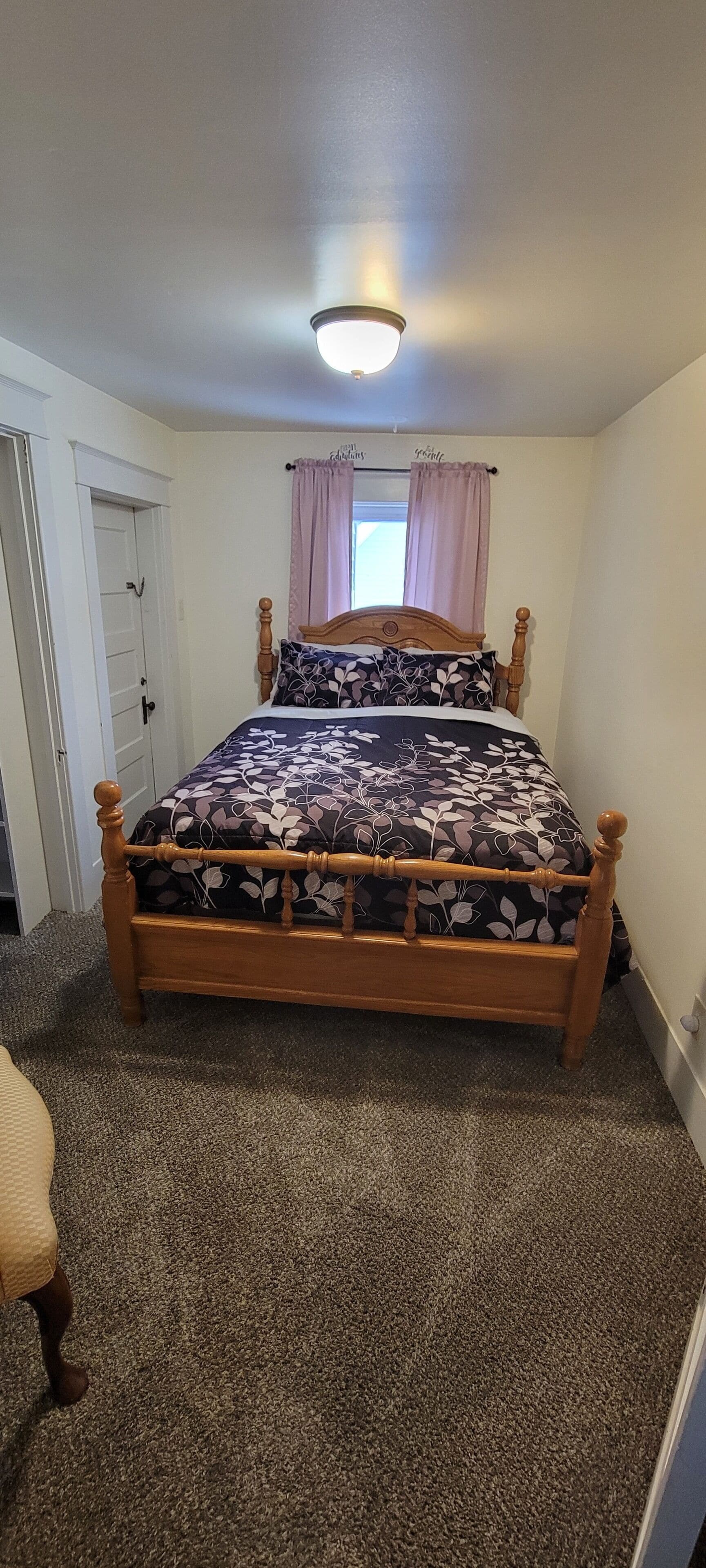 A bedroom with a wooden bed, a window with pink curtains, and a carpeted floor.