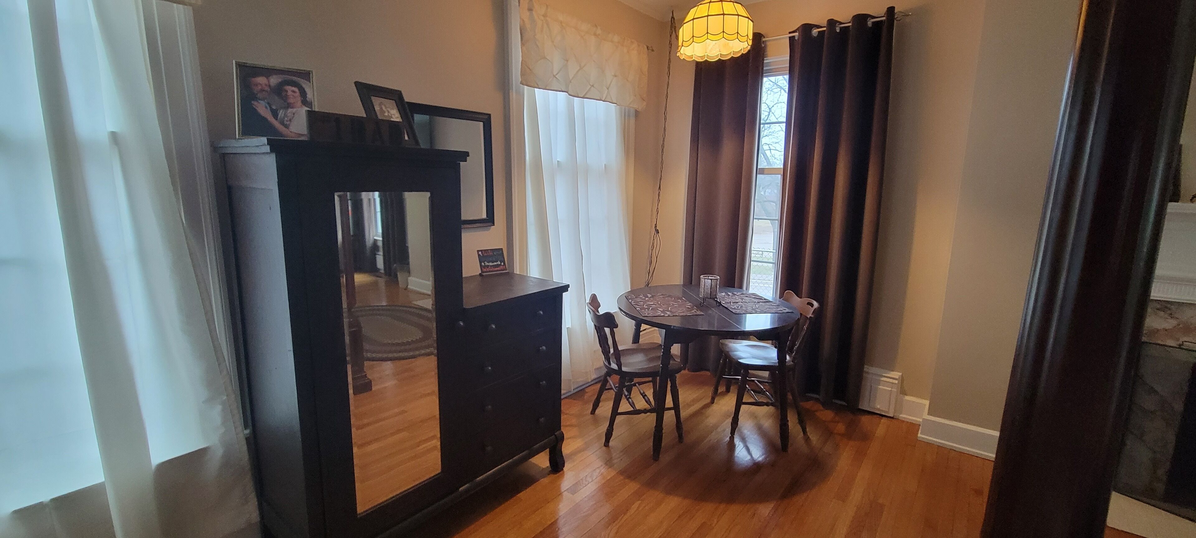 A dining area with a round table, chairs, a dark wooden cabinet, and a hanging light fixture.
