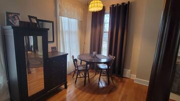 A dining area with a round table, chairs, a dark wooden cabinet, and a hanging light fixture.